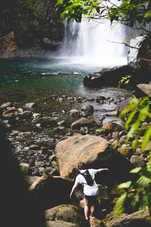 a person is sitting on rocks by a stream with waterfall