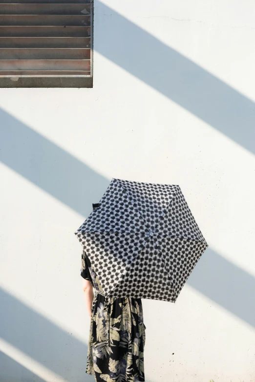 person under black and white umbrella looking towards wall