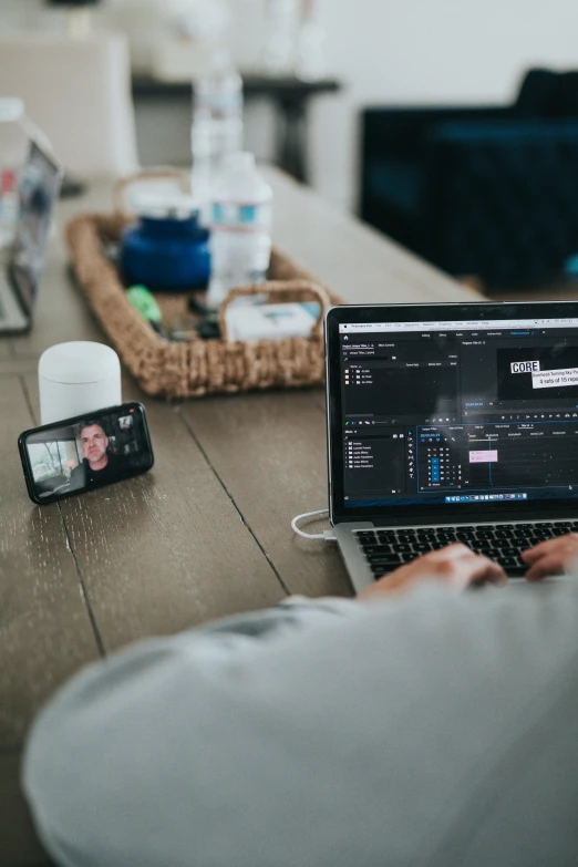 someone sitting at a table on his laptop with several electronic gadgets