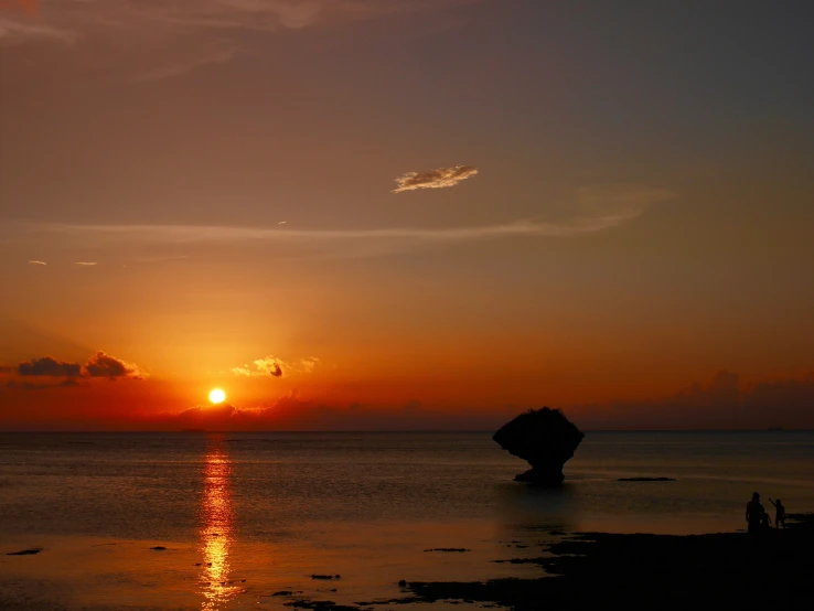 a large rock in the middle of the ocean with a sun setting in the distance