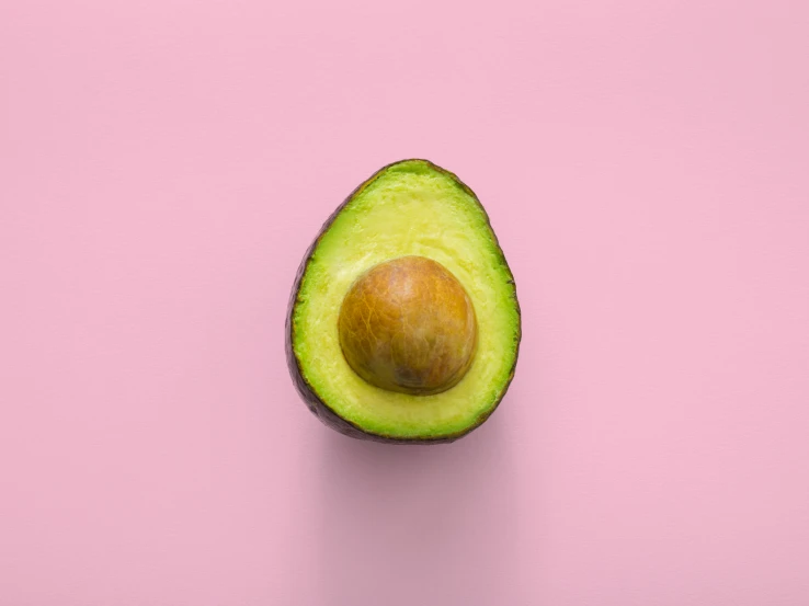 a half eaten avocado on a pink background