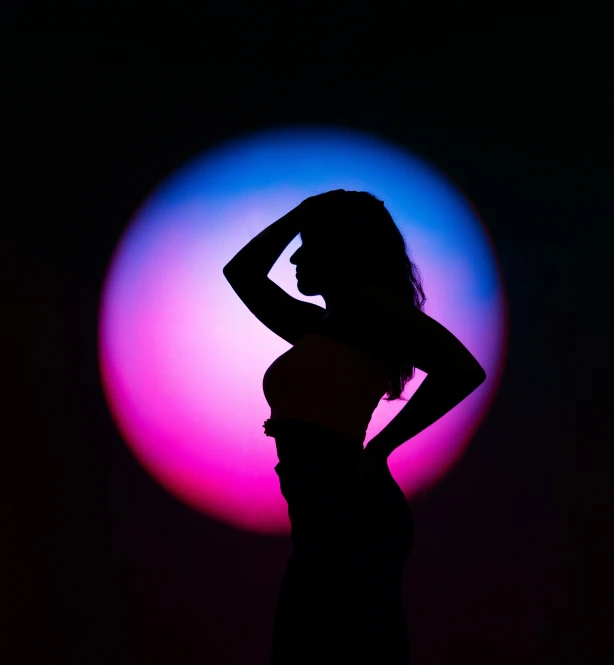 a dark silhouette of a young woman posing for a po in front of a colored ball