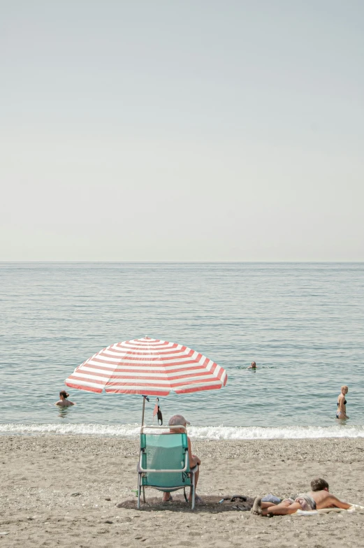 beach scene with couple sitting in chairs, a woman laying in the shade, and two people playing in the water