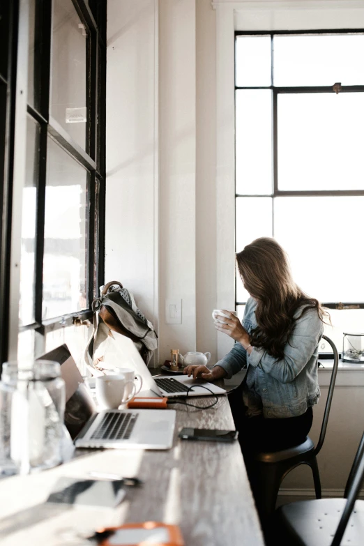 a woman sits in a chair at a desk next to a window and drinks