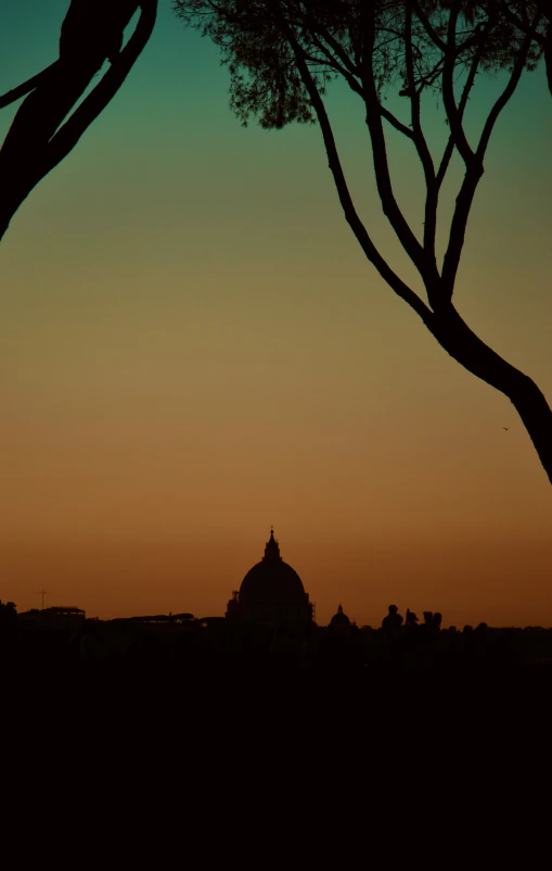 a silhouette of trees and buildings against an orange and blue sky