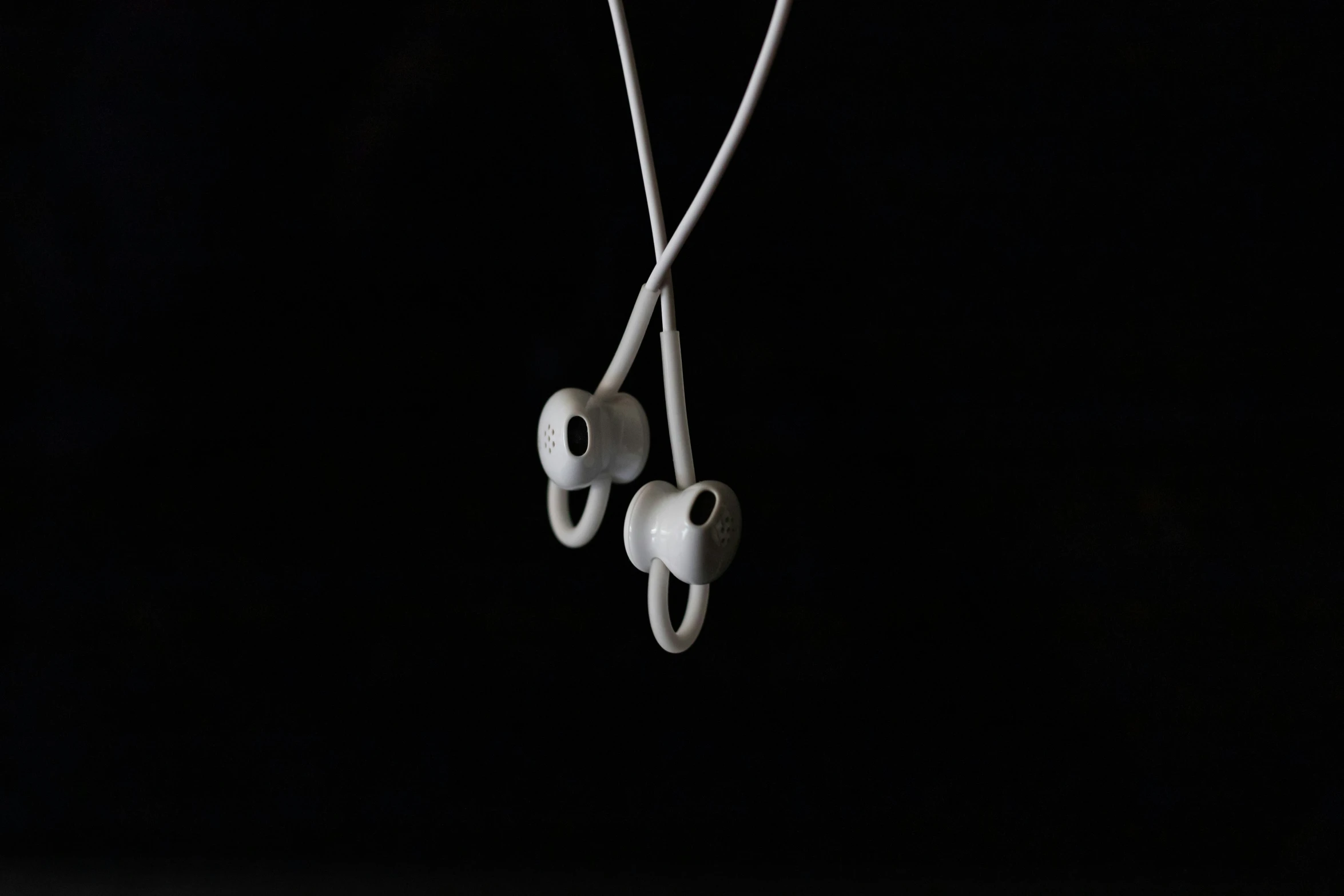 two ear buds hang off a string in the dark