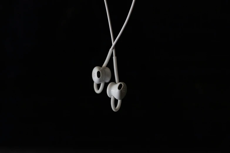 two ear buds hang off a string in the dark