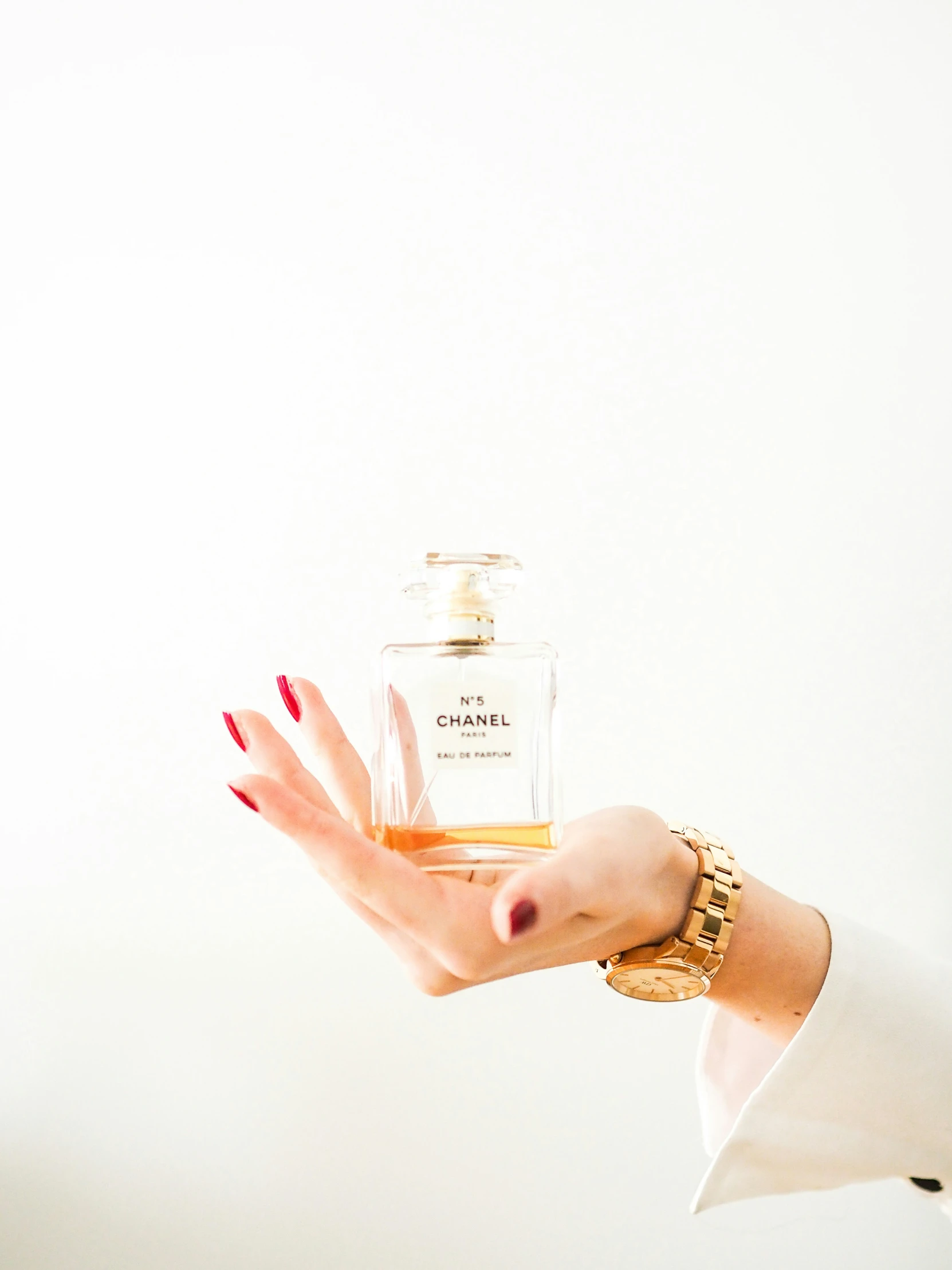 a woman holding a perfume bottle and red nails