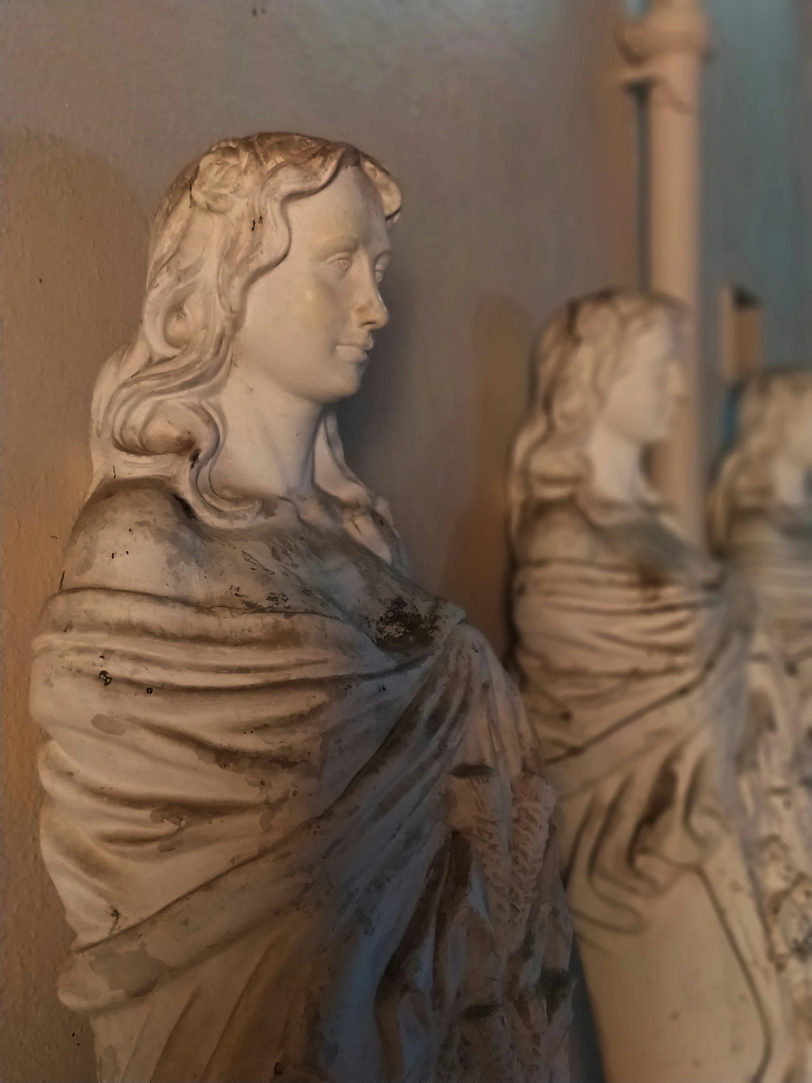 some statues sit next to a wall and a candle holder