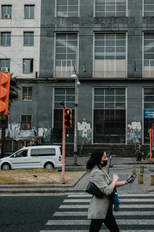 woman holding a smart phone crossing an intersection in front of buildings