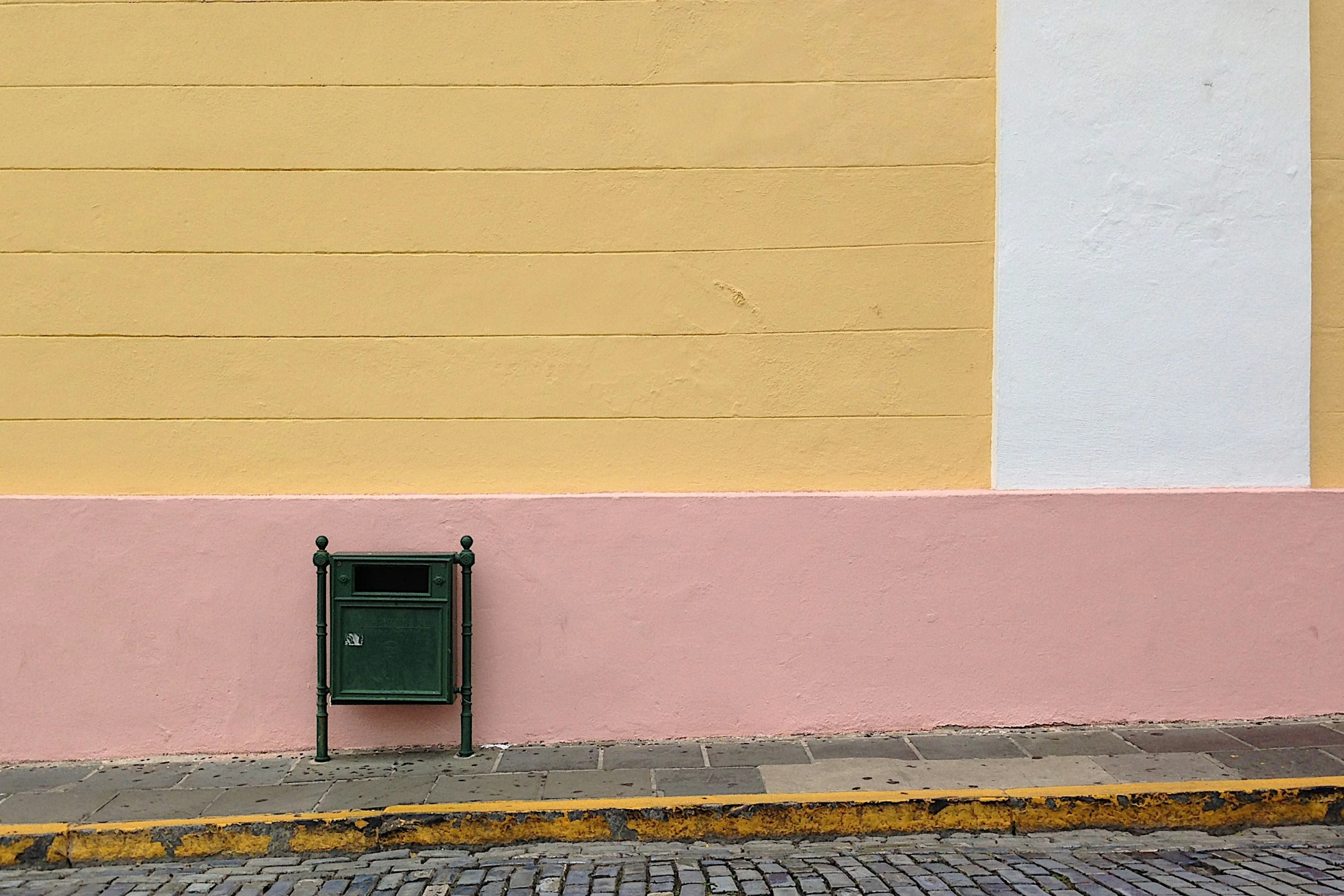 a black box sitting on the sidewalk near a large pink wall