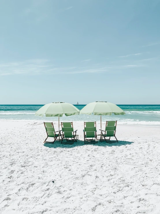 three lawn chairs and umbrella on a sandy beach