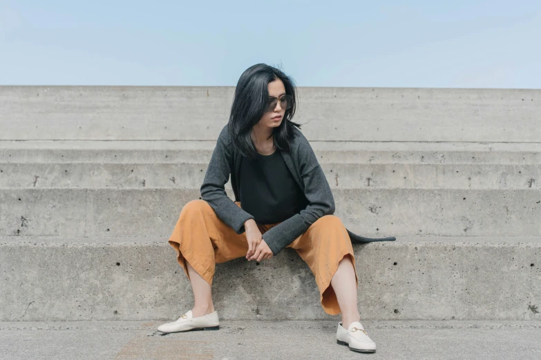 a woman is sitting on some stairs in a black shirt and orange pants