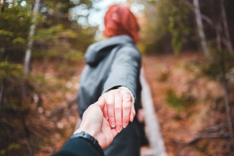 a woman with red hair holds the hand of a person in a black coat