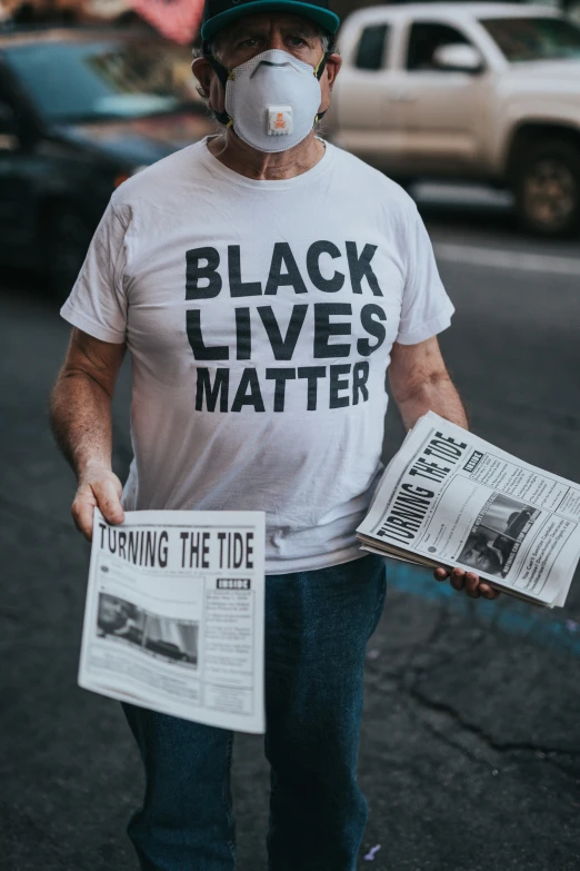 man wearing a white tee shirt reading a news paper and mask