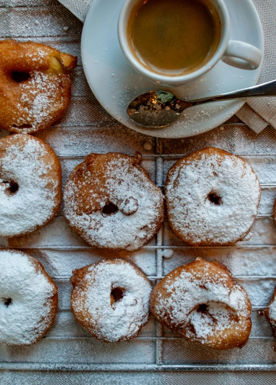 small round donuts are arranged on a rack and next to a cup of coffee