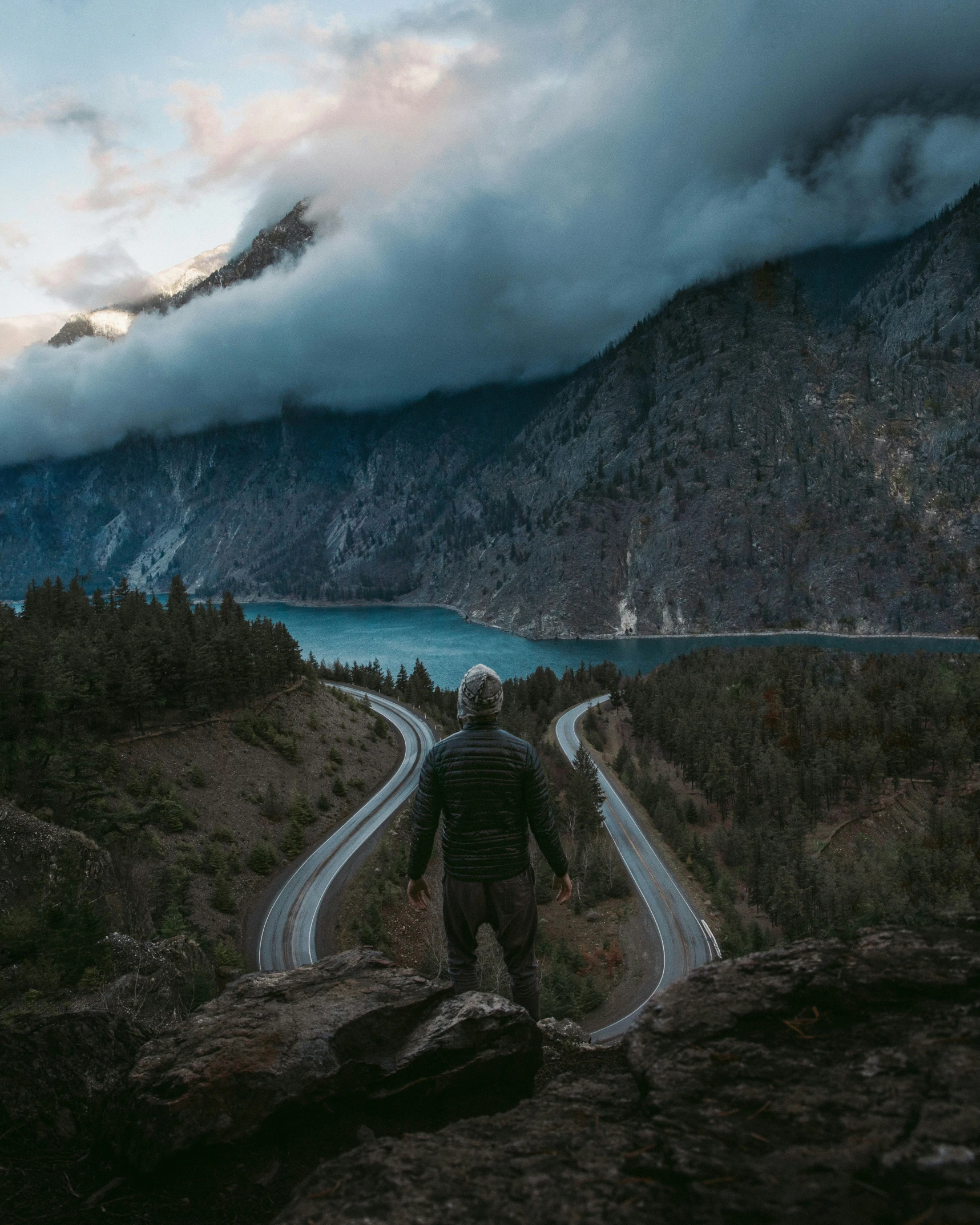 the man in the black jacket walks down the road to the lake