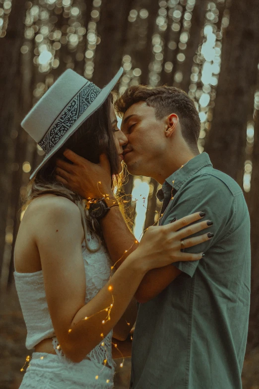 a man and a woman in a white dress kiss as they stand by a forest covered with lots of lights