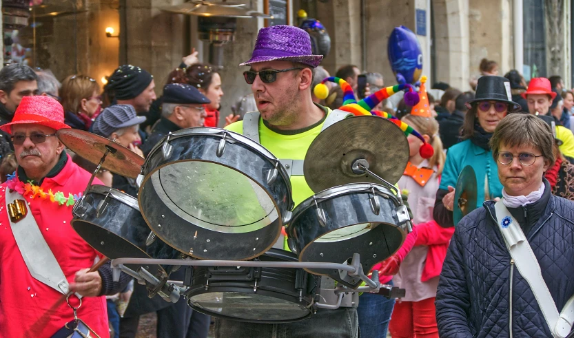 a man in yellow shirt and colorful hat carrying a drum set in parade