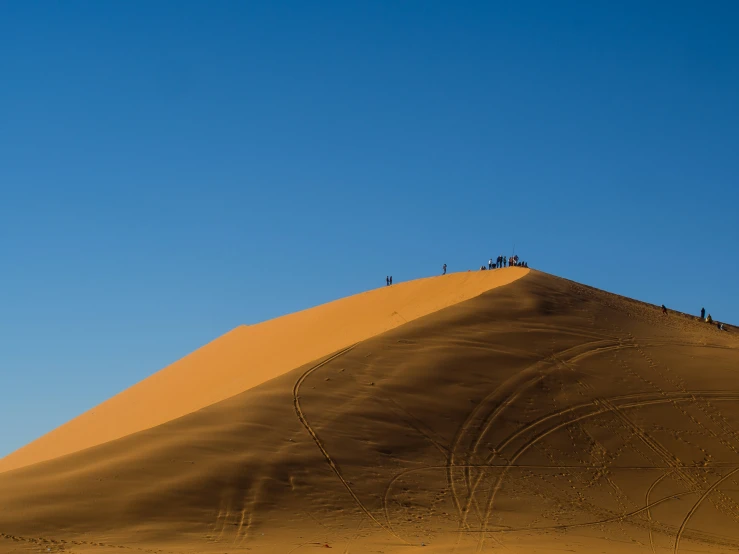 several people walking in the sand on top of a dune