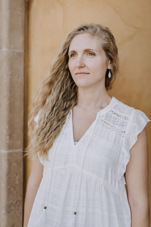 a woman standing with long, blonde hair looking at the camera