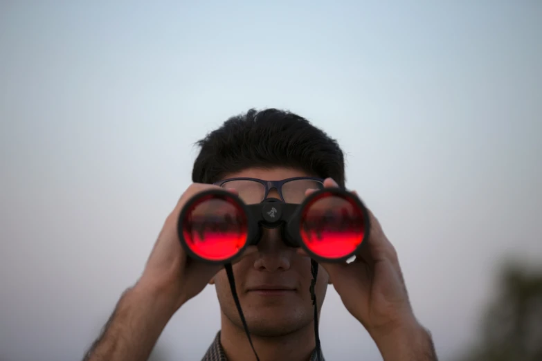 a young man standing with his hands to the sides of his eyes and looking through some binoculars