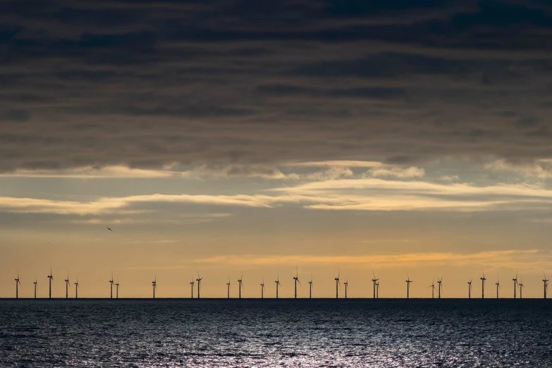 there are wind mills and clouds over the ocean