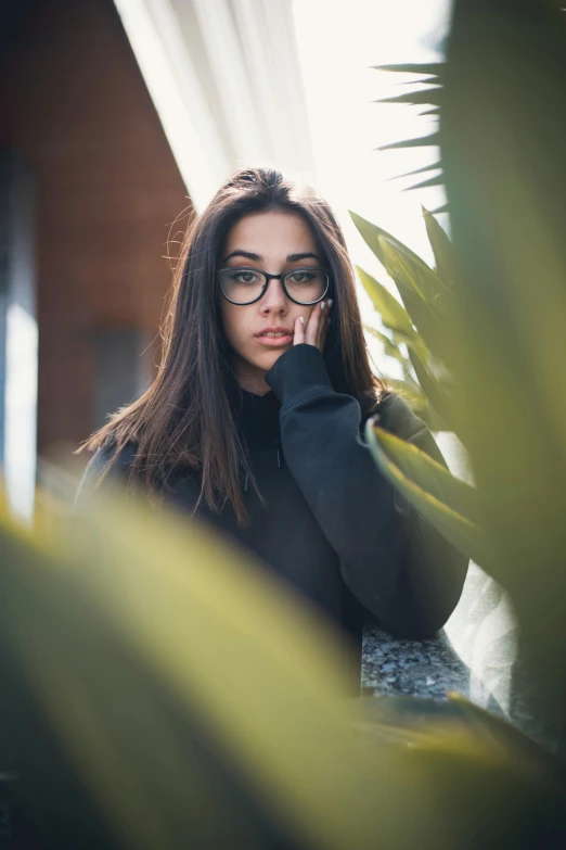 a woman with black glasses in front of plants