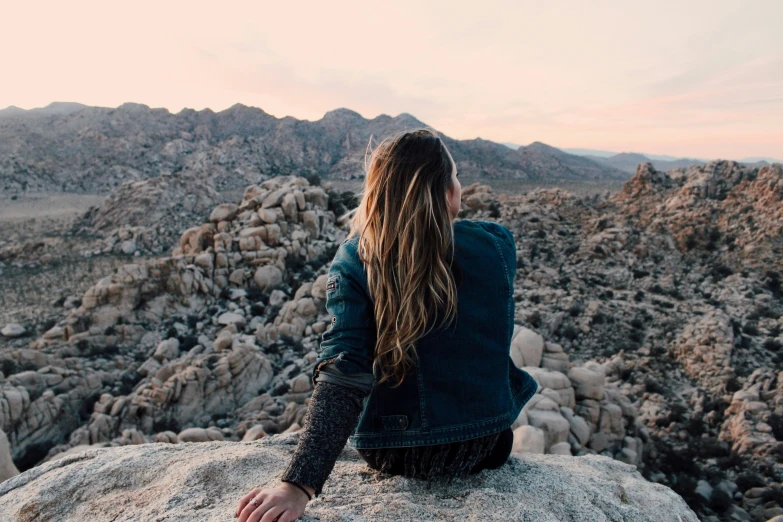 a person sitting on top of a large rock looking down at the landscape