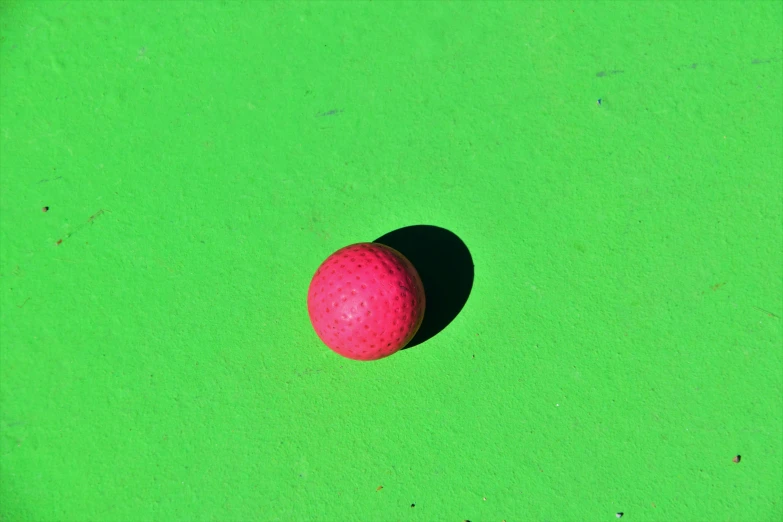 a red ball sitting on top of a green surface