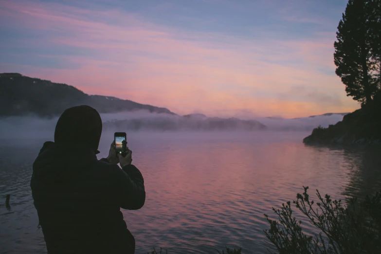 a man holding a cell phone up to a sunset