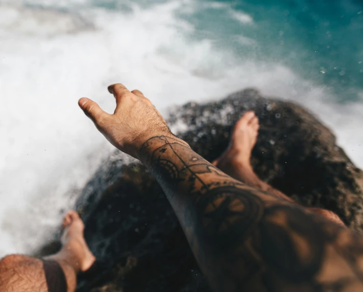 a person with tattoos standing on some rocks in the ocean