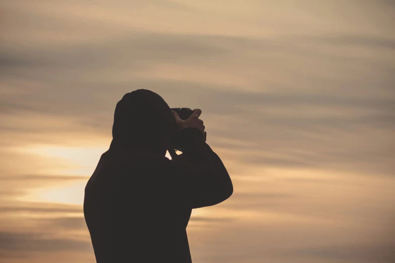 person taking pograph with camera phone at sunset