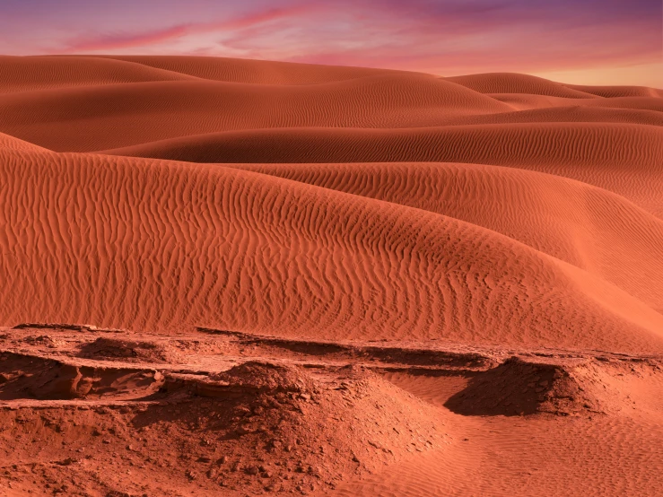 sand dunes and small rocks under an orange sunset