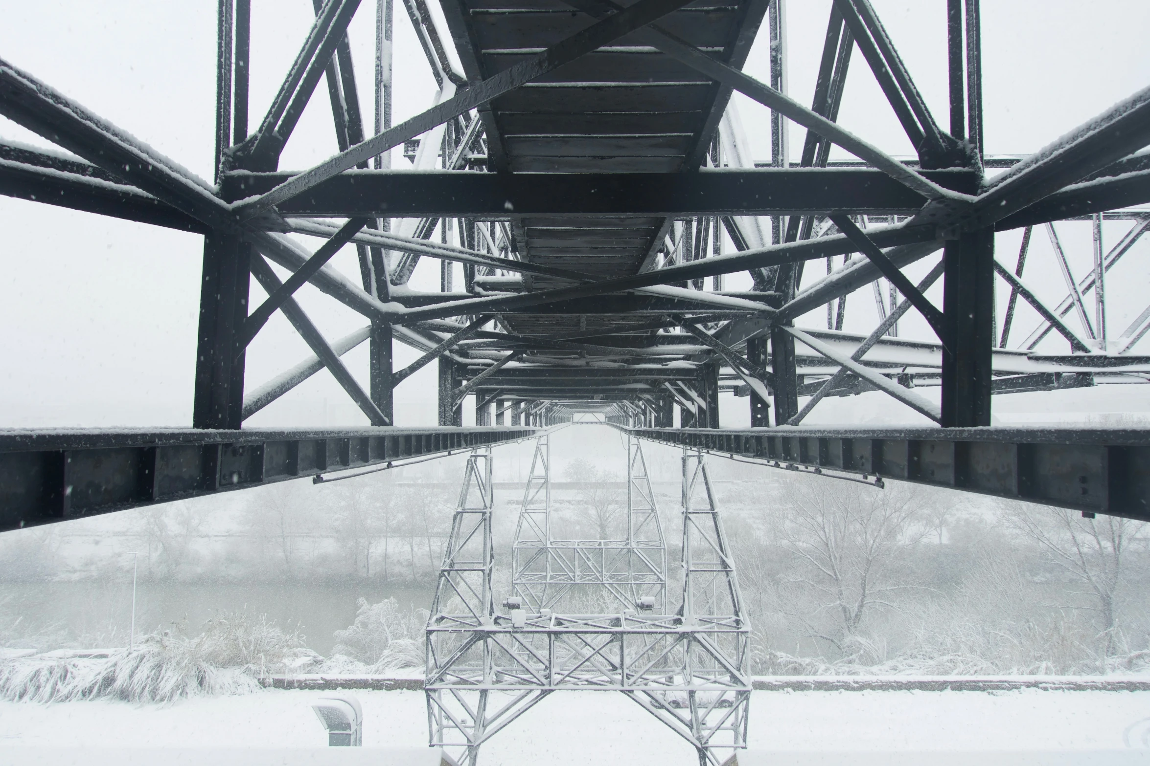 an old steel bridge with snow on the ground