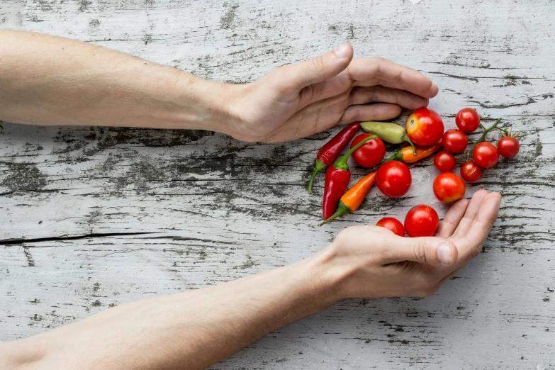 two hands are reaching for red tomatoes and a green pepper