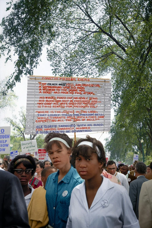 a group of women standing under a sign next to trees