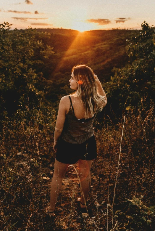 a woman is walking in tall grass at sunset