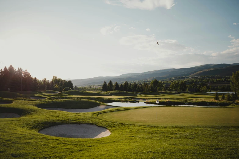 the golf field is shown in the sun with mountains behind it