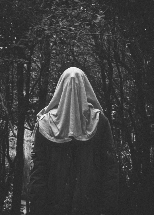 a hooded woman walking through a forest in the dark