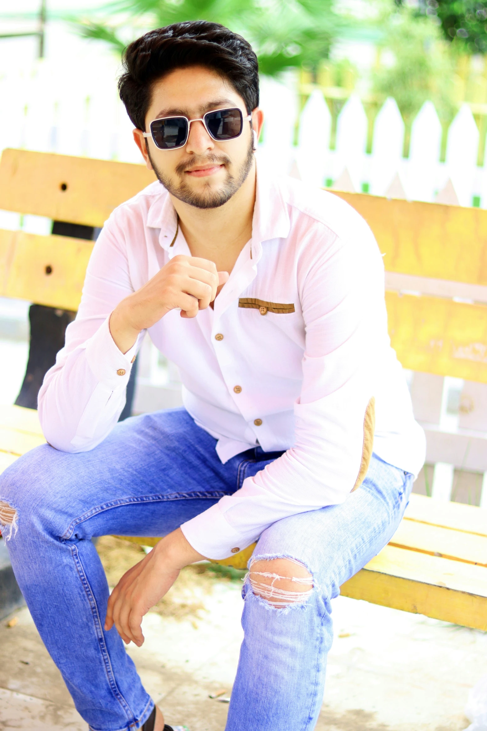 a man sits on top of a bench in ripped jeans