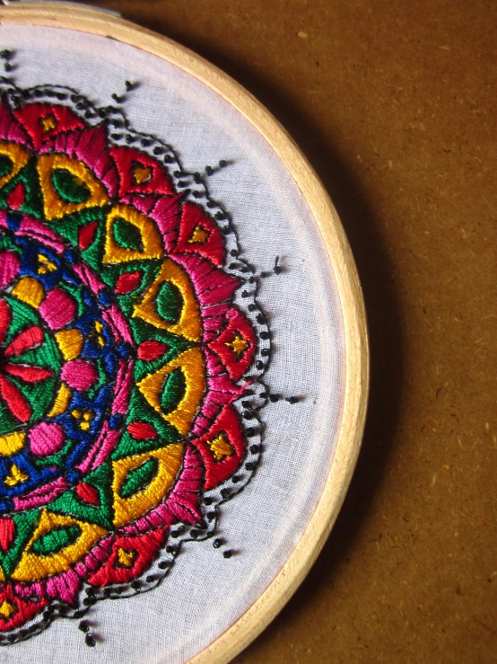 a colorful hand embroidered piece of art on a brown surface