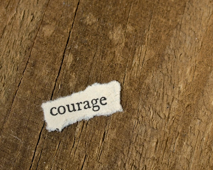 torn paper on wooden surface reading courage