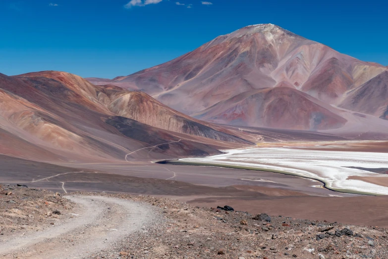 a view from atop a barren hill with white patches in the middle and brown mountains in the background