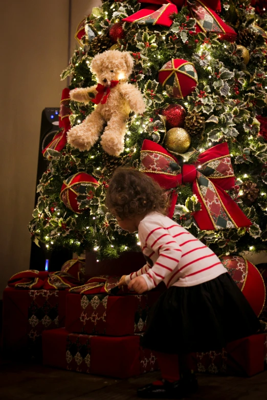 a child in striped shirt reaching towards gift under christmas tree