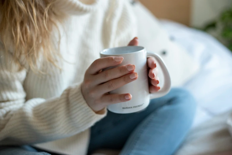 girl with nails holding a white cup on a bed