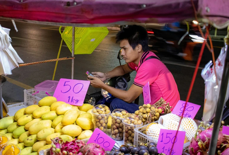 a person sitting down at an open air stand looking at her phone