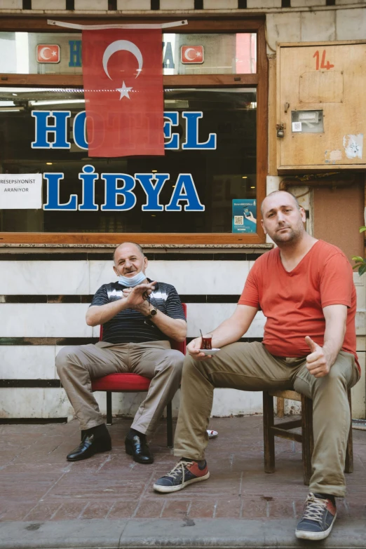 two people are sitting on a bench outside of a building