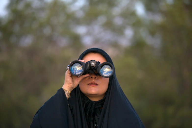 the woman is looking into binoculars through a black scarf