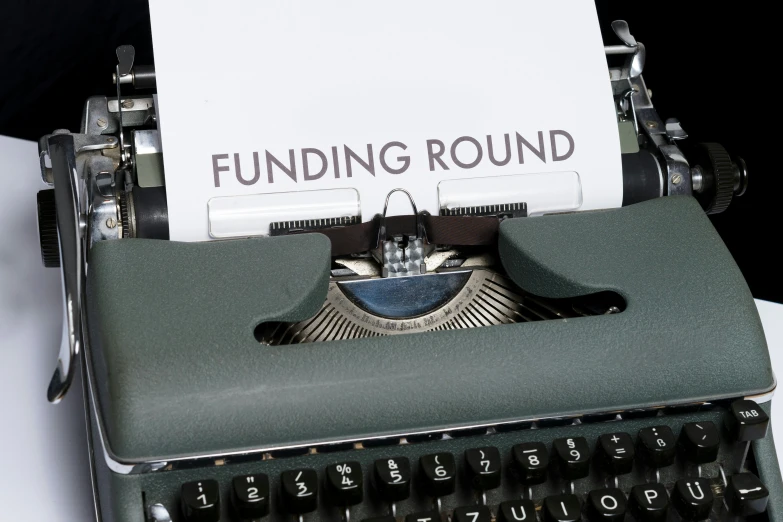 an old, green typewriter with paper with the word funding round